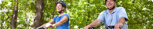 Man and woman riding bicycles on path in woods.