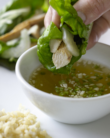 Person's fingers holding Asian-style chicken wrap over a bowl of sauce