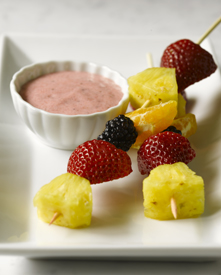 Two fruit skewers and a bowl of yogurt dip on a plate