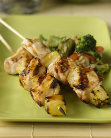 Two Hawaiian huli huli chicken skewers with vegetables on a plate