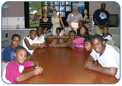 A group of children sits around a table with a row of adults standing behind them