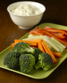 Broccoli florets and sliced carrots, celery, and red peppers on a plate with a side of dip in a bowl