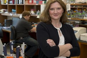 Photo of Dr. Beth Kozel in lab setting, arms crossed and smiling at camera